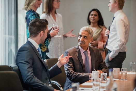 Two male businessmen having a conversation while sat at the conference table.