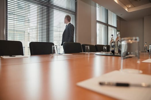 Young businessman waiting to have a meeting. Stood, looking out the window in the conference room.