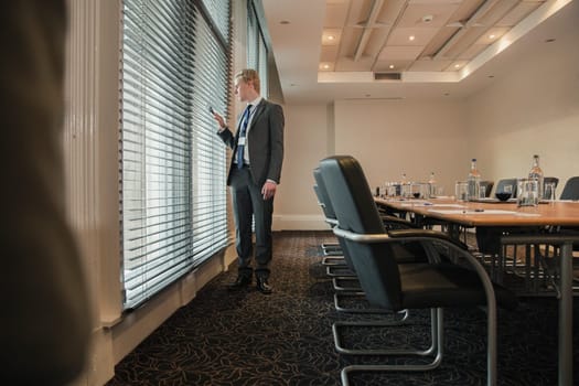 Businessman waiting in the board room for a meeting. Looking through the blinds and window to see if people are arriving.