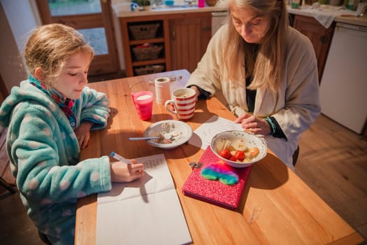 Mother and daughter sitting at the table in the kitchen. Mother is checking over her daughters homework before school.