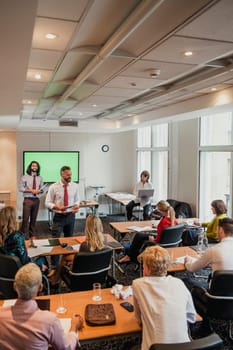 Mature male adult businessman giving a presentation at the front of the room while everyone is sat and listening.