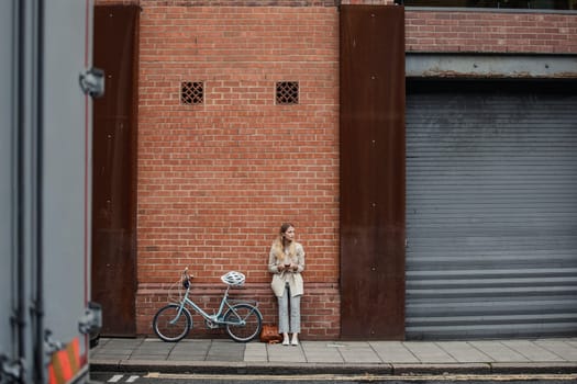 young businesswoman standing against a wall on her mornig commute to work and trying to kill some time.