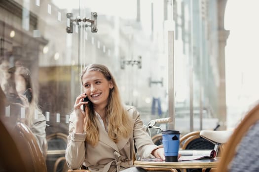 Front View of a young adult businesswoman making a phone call and having a coffee before work.