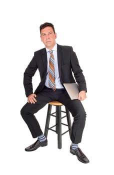 A middle age businessman sitting in a dark suit on a chair holding his.laptop in his hand, isolated for white background.