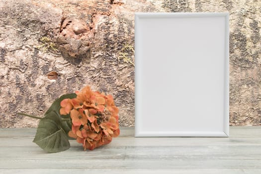 Photo frame with orange flower on wooden table and natural bright tree background. Place your text or photo. Concept card.