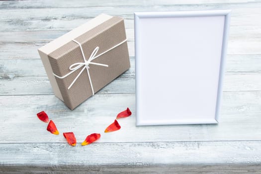 Gift box with a white picture frame with place for your text and tulip leaves on rustic bright wooden table. Card concept.