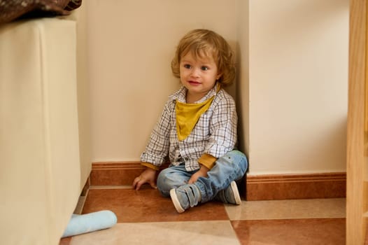 Young child indoors, seated in a corner, joyfully interacting. The playful environment and casual attire evoke innocence and comfort.