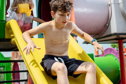 Young boy playing carefully on a plastic slide in a children playground park