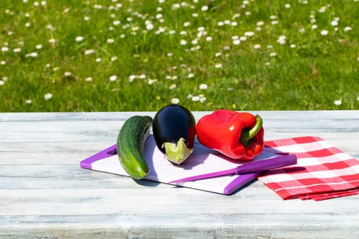 Fresh vegetables on rustic bright wooden table with natural green background. Courgette, cucumber and paprika are on a cutting board. Concept health.
