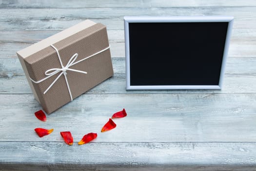 Gift box with an empty picture frame with place for your text and tulips leaves on rustic bright wooden table. Card concept.