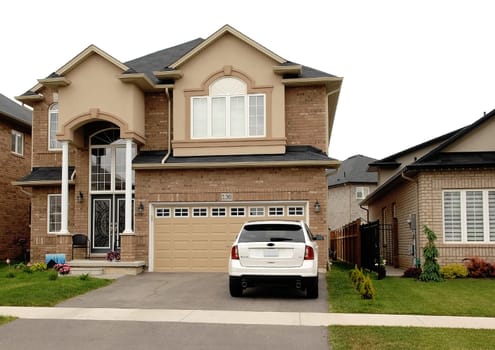 A new big house in a subdivision in Hamilton, Canada with a white car.sitting on the driveway.