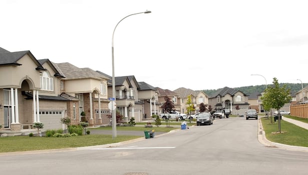 A suburban street with new big houses in the summer time whit cars.in the drive way.