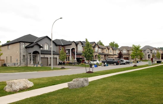 A suburban street with new big houses in the summer time whit cars.in the drive way.