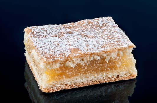 Piece of lemon pie. Black background with reflection.
