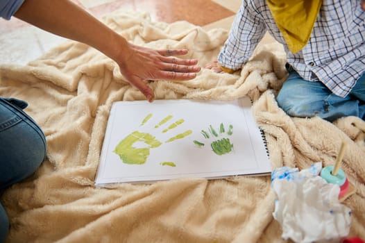 Creative activity on a soft blanket as adult and child enjoy painting handprints, symbolizing bonding, art, and fun.