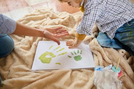 A mother and child enjoy creating colorful handprints together on paper during a bonding moment. Ideal for Children's Day and Mother's Day concepts, family art, and creativity.