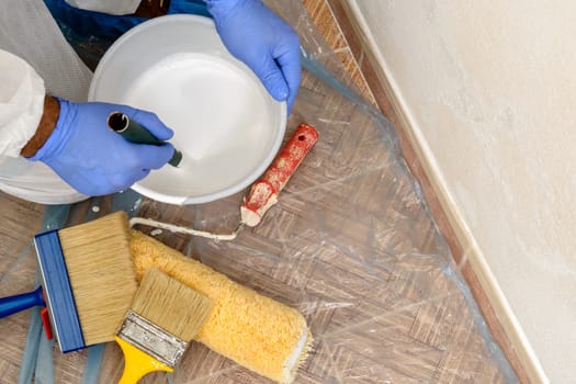 Painter paints the wall with the tint of white. Wall with serious moisture problems. Detail of the brush. white dye is prepared for the painter's job.