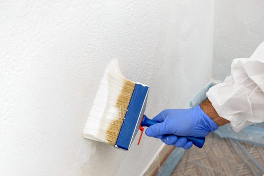 Painter paints the wall with the tint of white. Wall with serious moisture problems. Detail of the brush. white dye is prepared for the painter's job.