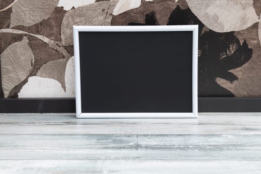 Front view black photo frame on wooden ground in front of wallpaper.