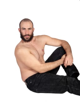 A sexy handsome man without a shirt sitting in black jeans on the.floor relaxing after some exercises, isolated for white background.