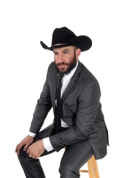 A handsome man sitting in a gray suit and cowboy hat looking away,.with beard and mustache, isolated for white background.