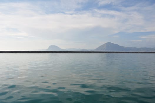 Distant hills sea and cloudy sky horizon landscape. Seawall pier on port of Patras, Greece.