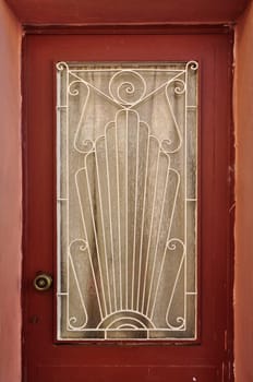 Old wooden door glass lite screen decorated with iron pattern of abstract sun rays and spiral symbols.
