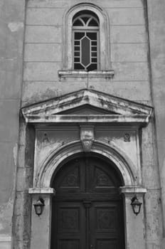 Byzantine church exterior with alpha and omega engraved inscription. Arched wooden gate and weathered wall black and white.