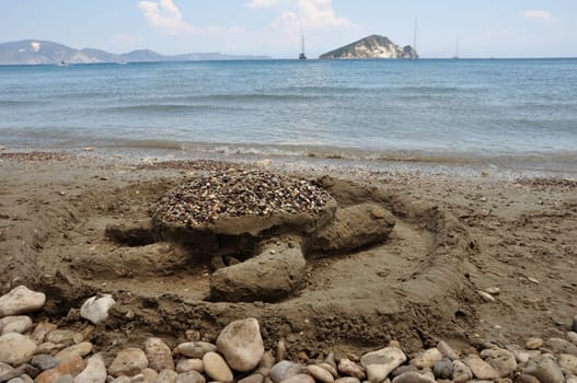 Loggerhead sand sculpture on Keri beach and distant view of Marathonisi islet shaped like a gigantic sea turtle and favorite nesting ground of the caretta caretta. Zakynthos, Greece.