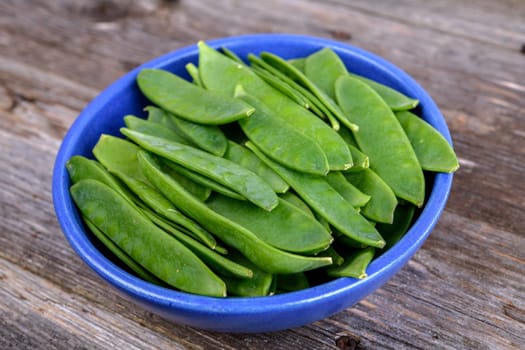 blue bowl with green peapods  on wooden ground