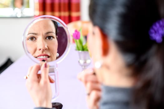 young dark haired woman looking in mirror and applying make up