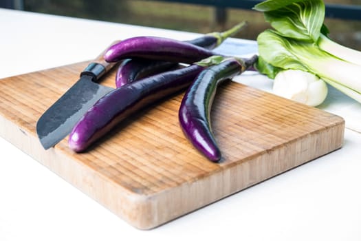 japanese eggplant on wooden board with cooking knife and pak choi salad