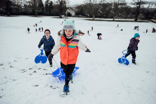 Children from the community are running up a hill to have a race together on sleds in the snow.