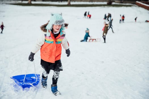 Little girl is walking up a hill, pulling her sled in the snow.