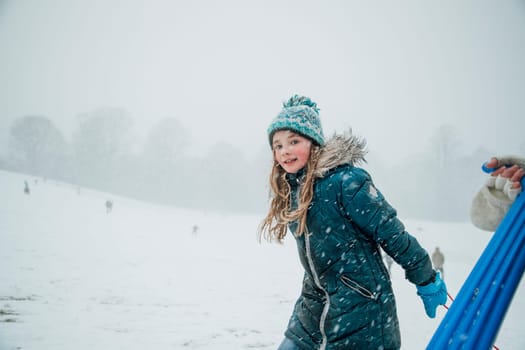 Little girl is looking at the camera while heading uphill with her friends to have a sled race.