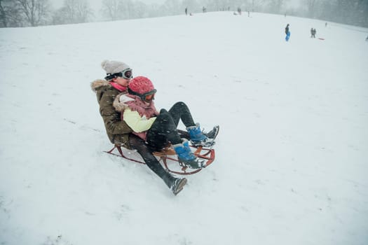Two girls are holding on to each other as they go down a hill together on a sleigh.
