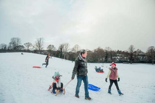Man is out sledding in the snow with his daughters.