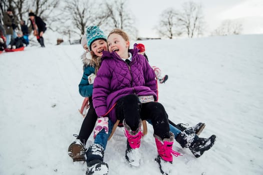 Three little girls are sitting on a sled together, going down a hill in the snow.
