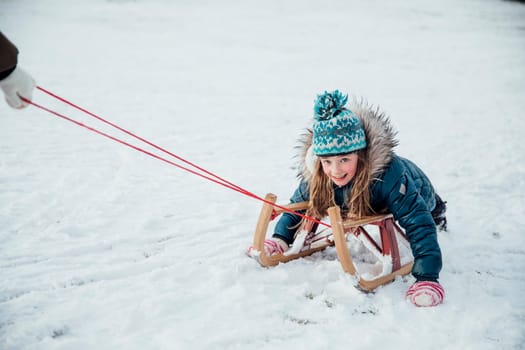 Little girl is smiling for the camera while being pulled on a sleigh in the snow.