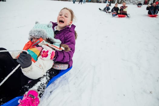 Children from the community are having a sled race in the snow on a big hill in a public park.