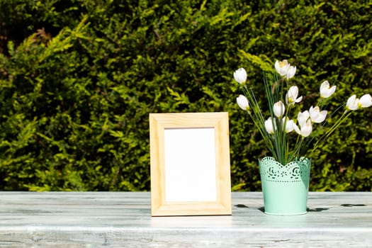 Empty wooden frame and white wild flowers on rustic bright wooden table over natural green background. Space.