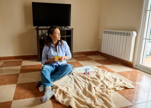 A woman sitting on a blanket enjoying a casual moment with toys, emphasizing warmth, simplicity, and connection.