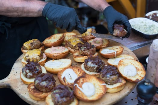 Chef making beef burgers outdoor on open kitchen international food festival event. Street food ready to serve on a food stall.