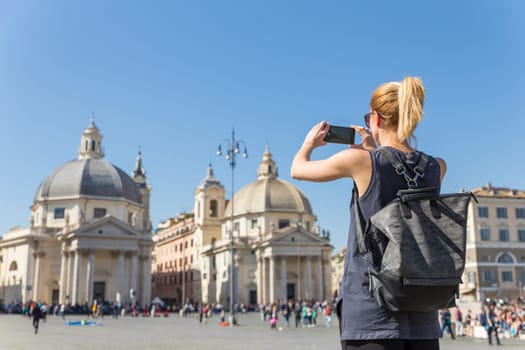Female tourist with a fashinable vintage hipster backpack taking photo of Piazza del Popolo, People's Square, in Rome, Italy by her mobile phone.