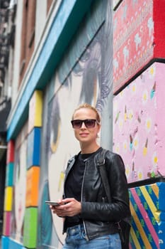 Closeup of female hipster with smart phone. Woman using smartphone against colorful graffiti wall in East Village, New York city, USA.