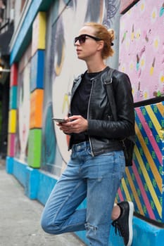Closeup of female hipster with smart phone. Woman using smartphone against colorful graffiti wall in East Village, New York city, USA.