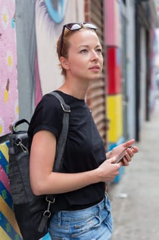 Closeup of female hipster with smart phone. Woman using smart phone app guite on city break weekend trip to East Village, New York city, USA.