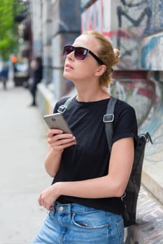 Closeup of female hipster with smart phone. Woman using smartphones against colorful graffiti wall in East Village, New York city, USA.