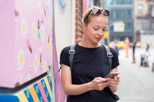 Closeup of female hipster with smart phone. Woman using smartphone against colorful graffiti wall in East Village, New York city, USA.