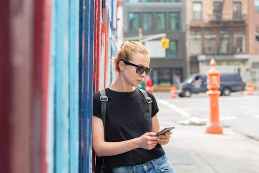 Closeup of female hipster with smart phone. Woman using smartphones against colorful graffiti wall in East Village, New York city, USA.